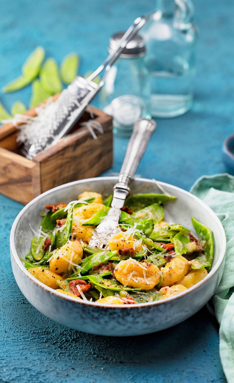 Gnocchi mit Zuckerschoten und getrockneten Tomaten in Parmesansauce angerichtet auf einem tiefen Teller