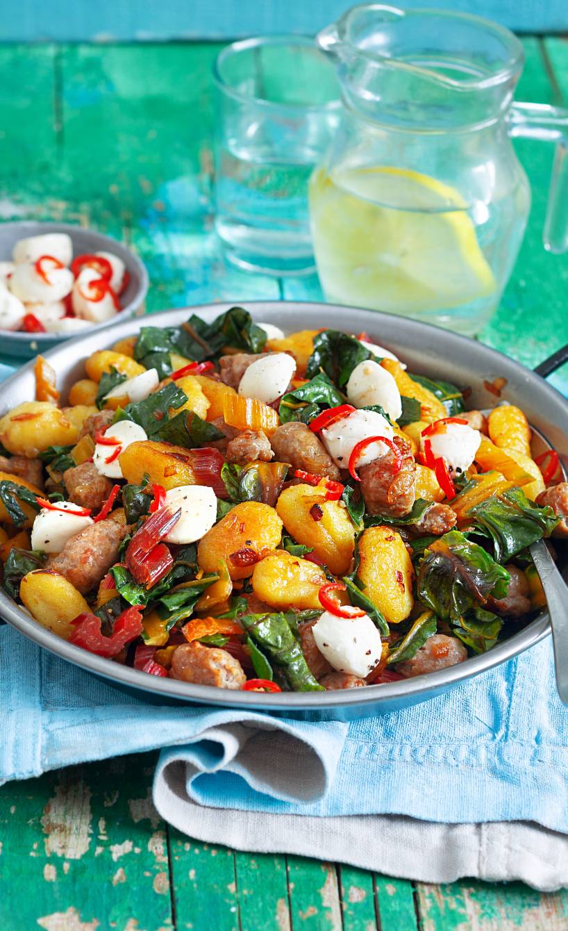 Mangold-Pfanne mit Gnocchi und Bratwurst in einer Pfanne auf einem türkisen Holztisch