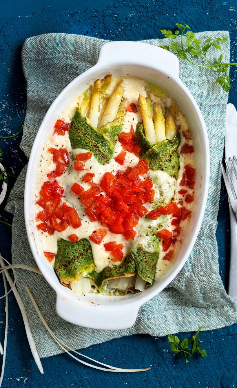 Überbackene italienische Kräuter-Crespelle mit weißem Spargel, Béchamelsoße und Tomatenwürflen in einer Auflaufform