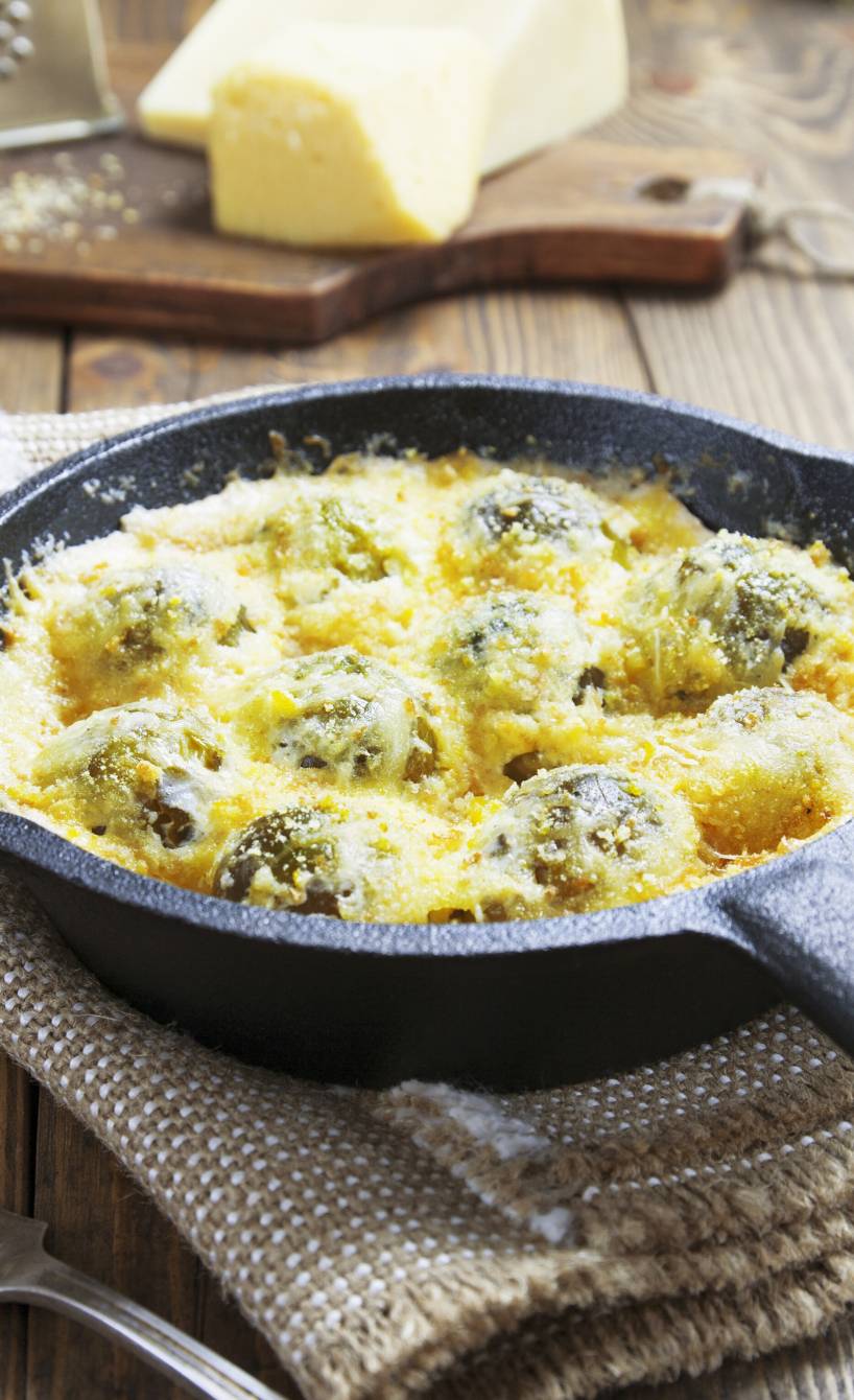 Rosenkohlgratin in einer Pfanne auf einem Tisch, daneben Parmesan am Stück