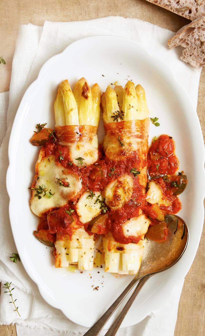 Zwei Pakete überbackene Spargel-Schinken-Röllchen in Tomatensoße mit Mozzarella auf einer Servierplatte