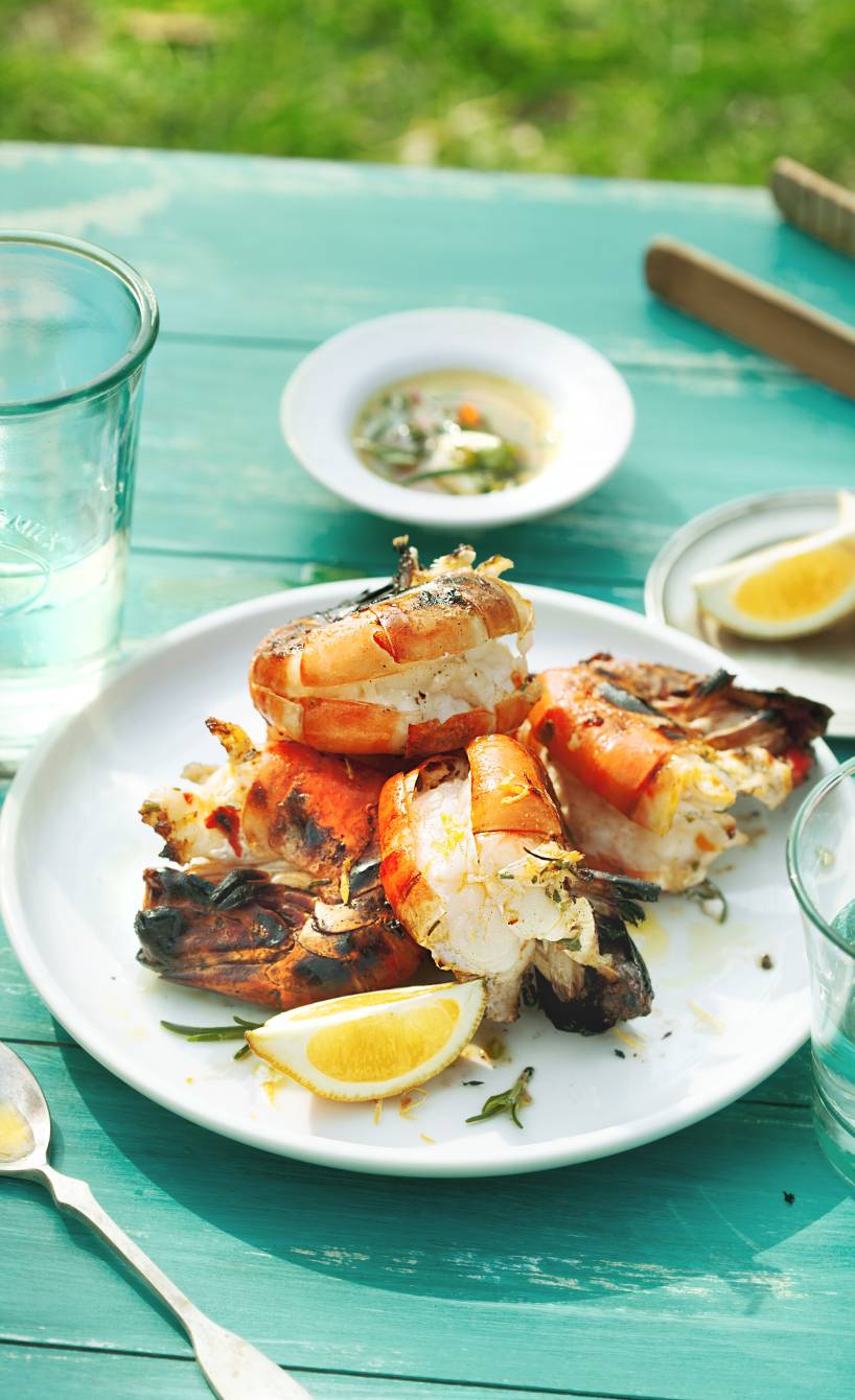 Gegrillte ganze Garnelen auf einem Teller, daneben Zitronen und eine Schüssel Marinade