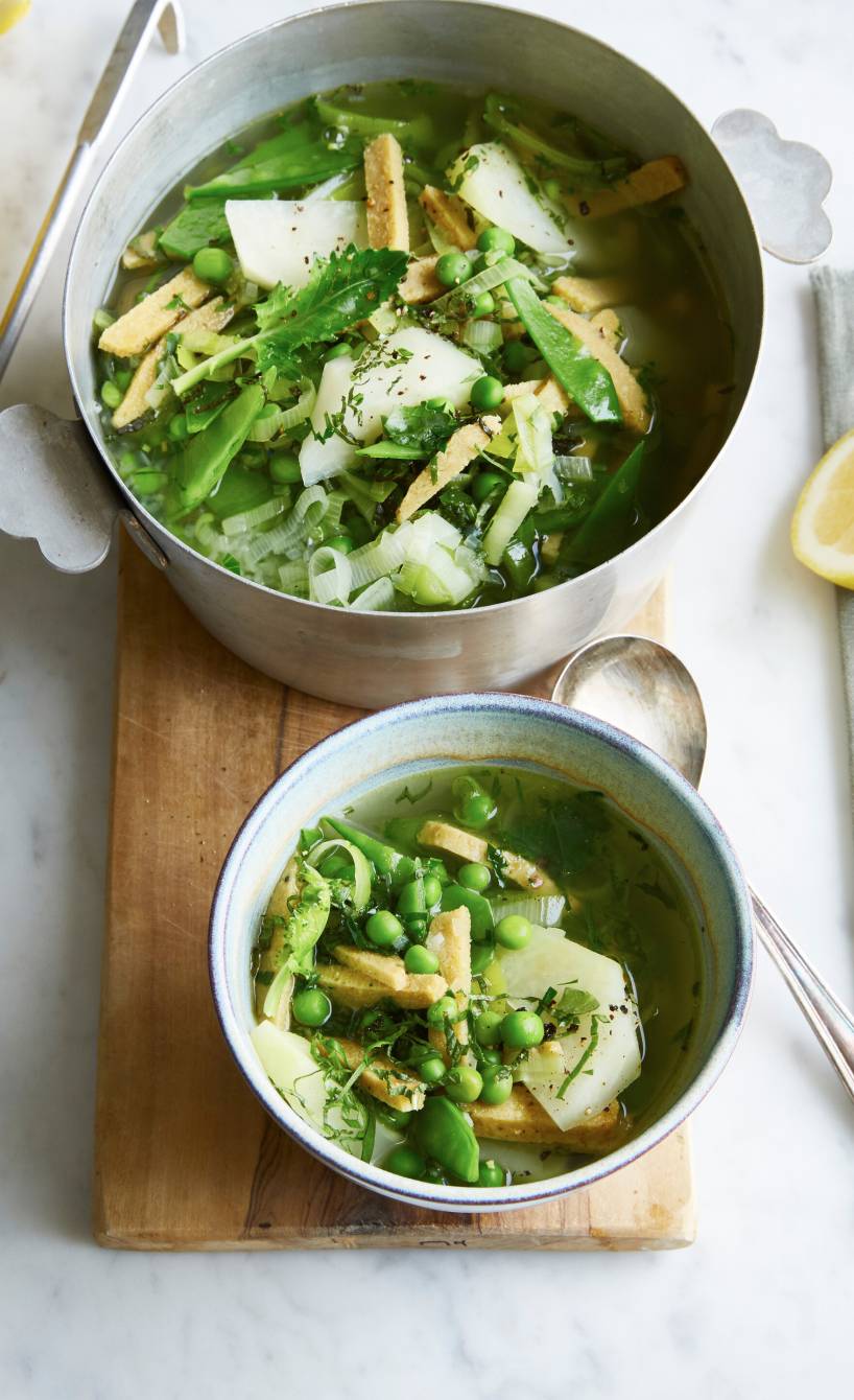 Grüne, vegane Minestrone mit Lupinenfilet in einem Topf und einer Suppenschale auf einem Tisch