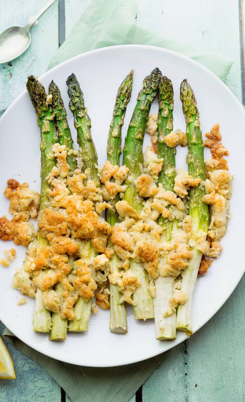 Grüner Spargel aus dem Ofen in ganzen Stangen auf einem Teller getoppt mit Parmesanstreuseln, daneben Joghurtdip in einer Schale