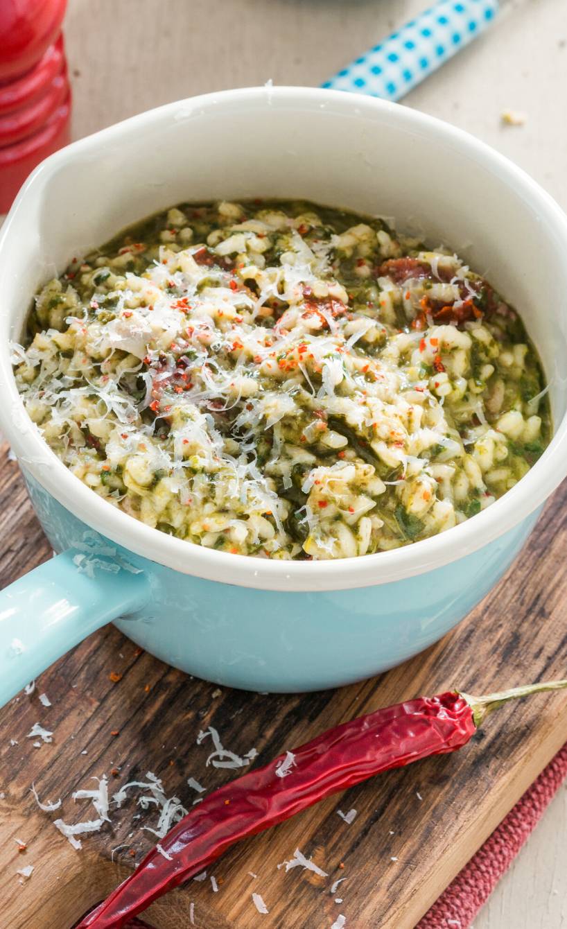 Grünkohlrisotto mit Pancetta, getrockneten Tomaten und Parmesan in einem kleinen Stieltopf auf einem Tisch