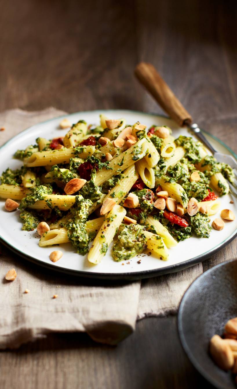 Nudelpfanne mit Grünkohl, grünem Pesto, getrockneten Tomaten und Mandeln angerichtet auf einem Teller