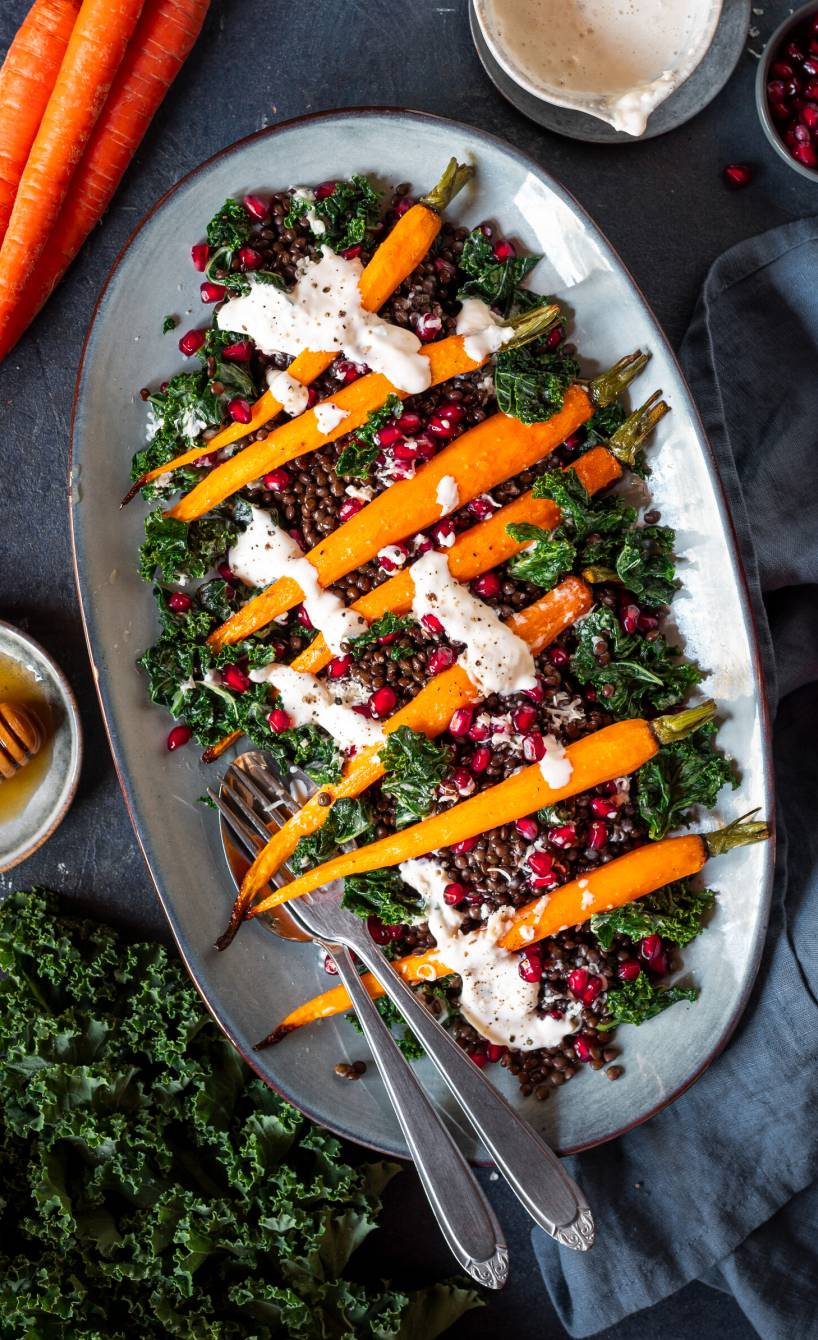 Grünkohlsalat mit gebackenen Karotten, Granatapfelkernen, Linsen und Crème fraîche-Parmesan-Dressing auf einem ovalen Teller angerichtet
