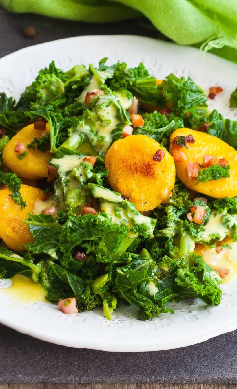Grünkohlsalat mit Kürbisnocken auf einem Teller, daneben Dressing