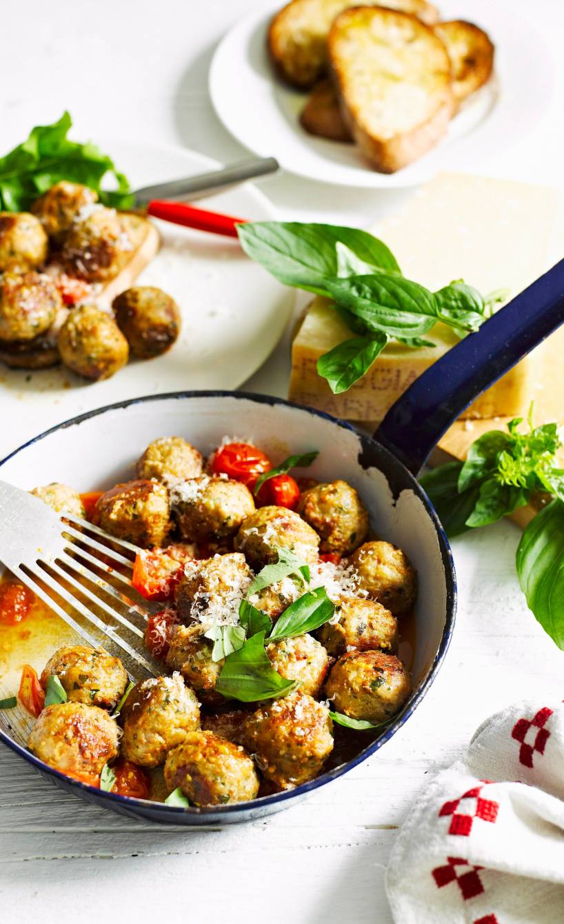Pfanne mit Hackbällchen und Kirschtomaten garniert mit Basilikum auf einem Tisch