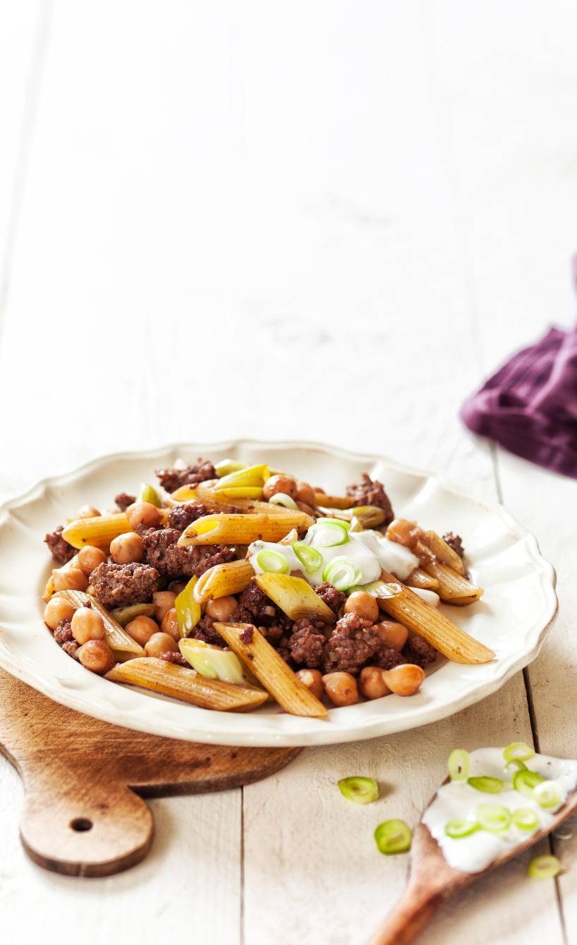 Nudel-Hackfleisch-Pfanne angerichtet auf einem tiefen Teller, getoppt mit saurer Sahne und Frühlingszwiebelringen