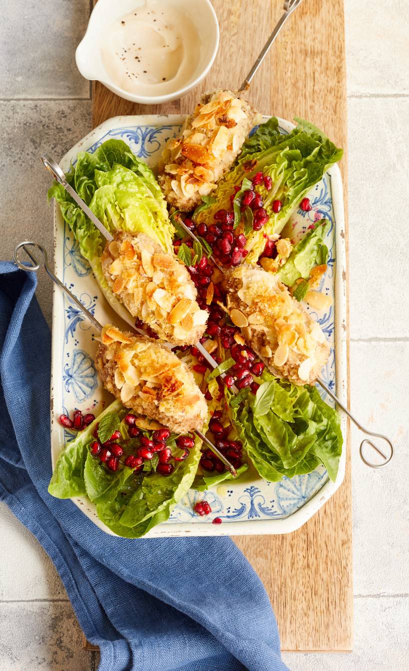 Vier gebackene Low-Carb-Hackspieße mit Mandel-Panko-Kruste angerichtet auf einer Platte mit Granatapfel-Minz-Salat