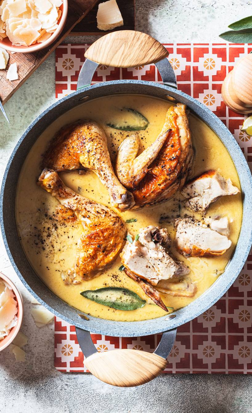 Hähnchenteile in einem Schmortopf mit Käse-Sahne-Soße und Salbeiblättern