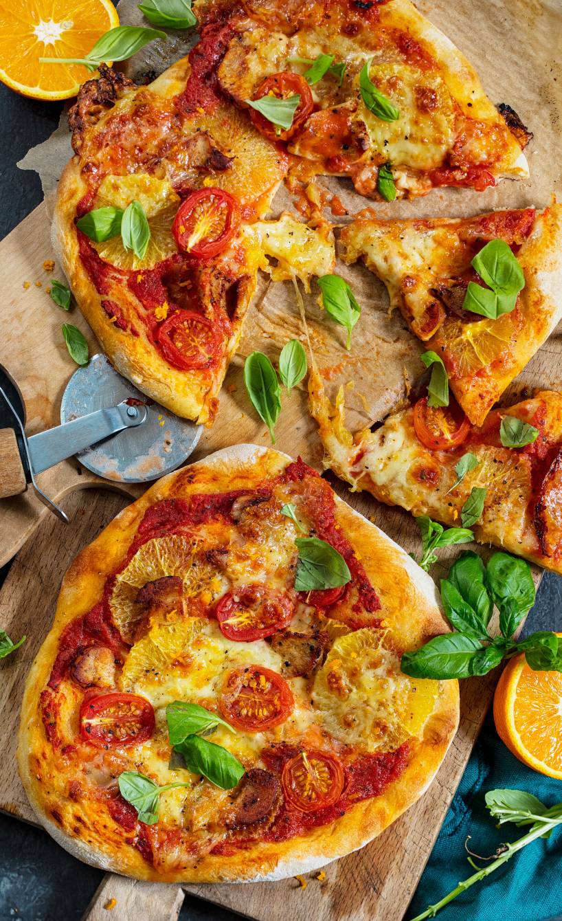 Zwei runde Pizzen mit Hähnchen-Orangen-Belag und Mozzarella auf Holzbrettern von oben