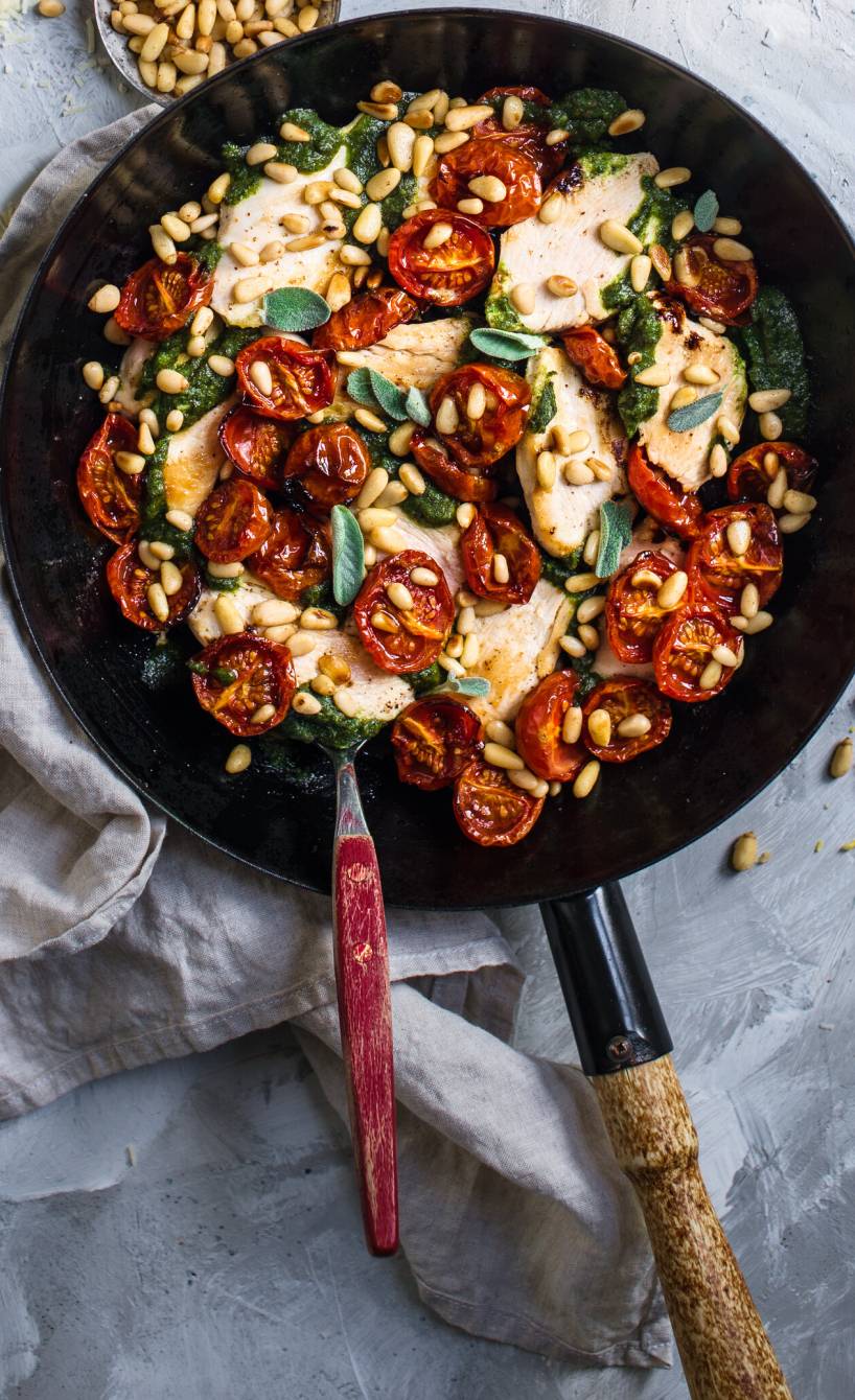 Hähnchen-Scaloppine in einer Pfanne mit Ofentomaten und Salbei-Pesto bestreut mit gerösteten Pinienkernen