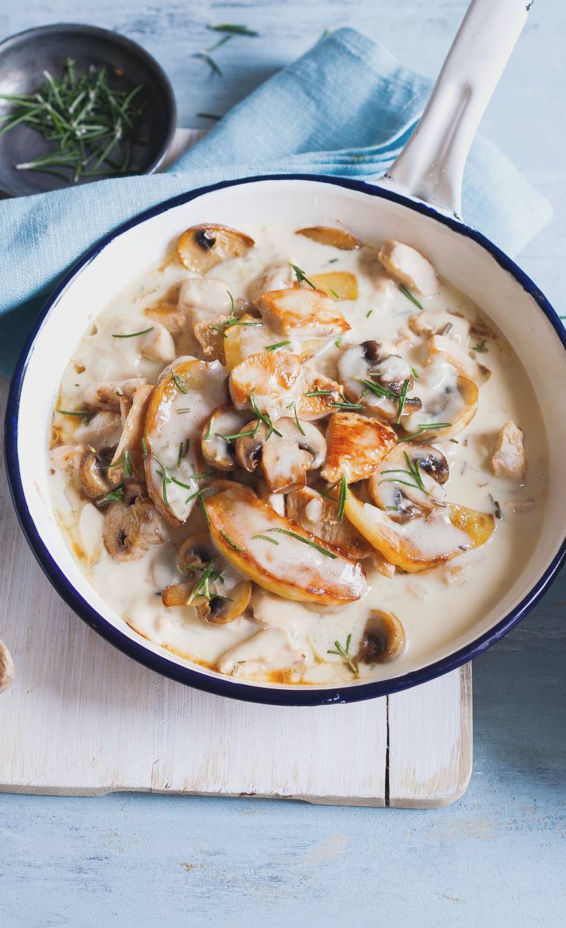 Hähnchenragout in Sahnesauce in einer Pfanne mit Champignons und Apfelspalten