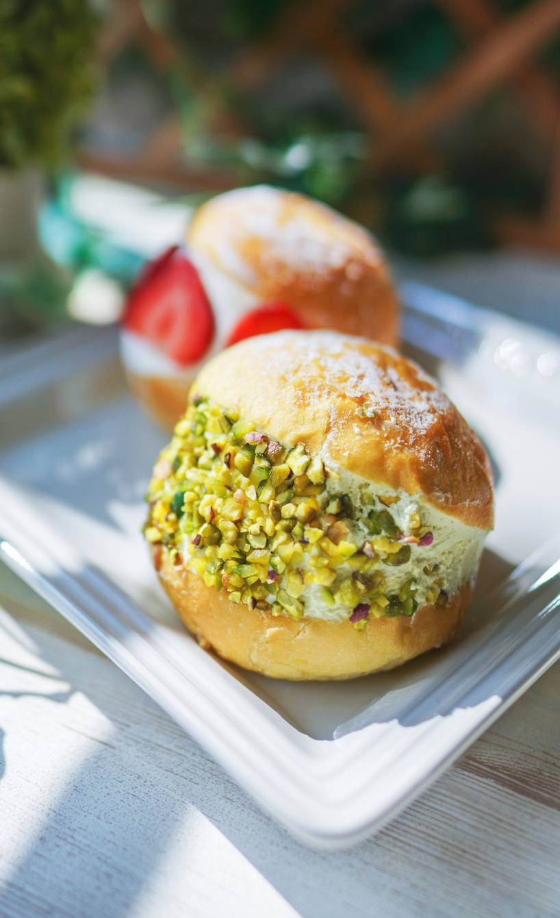 Zwei selbstgebackene Maritozzi Hefebrötchen gefüllt mit Sahne,  eines getoppt von Erdbeeren, eines mit Pistazien