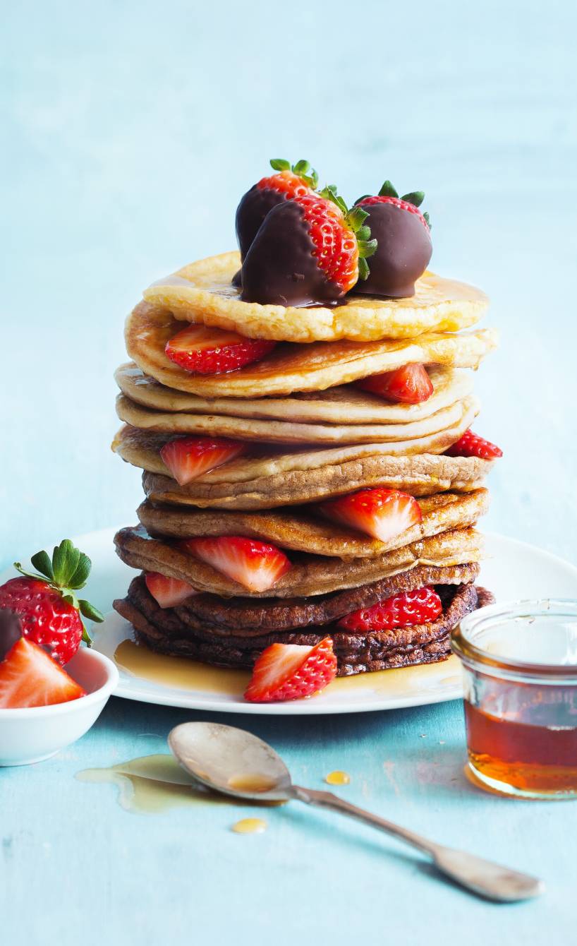 Helle und dunkle Pfannkuchen abwechselnd aufgetürmt auf einem Teller, daneben Erdbeeren mit Schokomantel