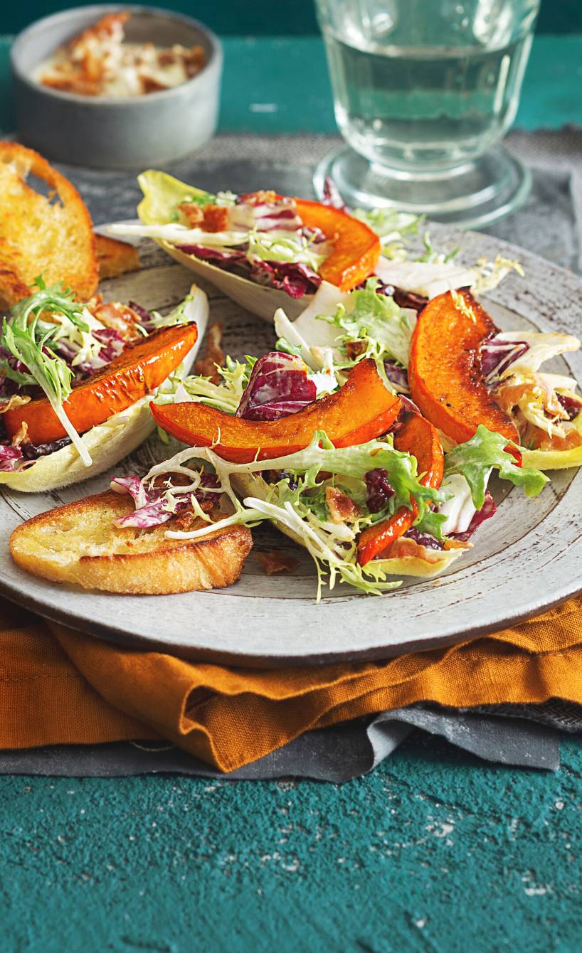 Herbstlicher Salat angerichtet mit Kürbisspalten und Ciabatta auf einem Teller