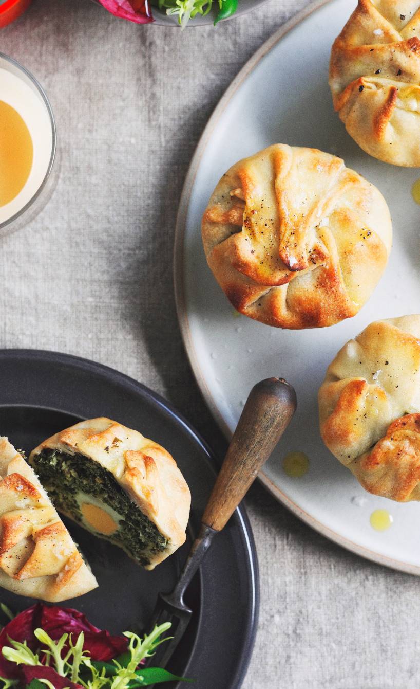 Herzhafte Mini-Osterkuchen auf einem Teller, daneben eines aufgeschnitten mit Füllung aus Spinat, Ricotta und Ei