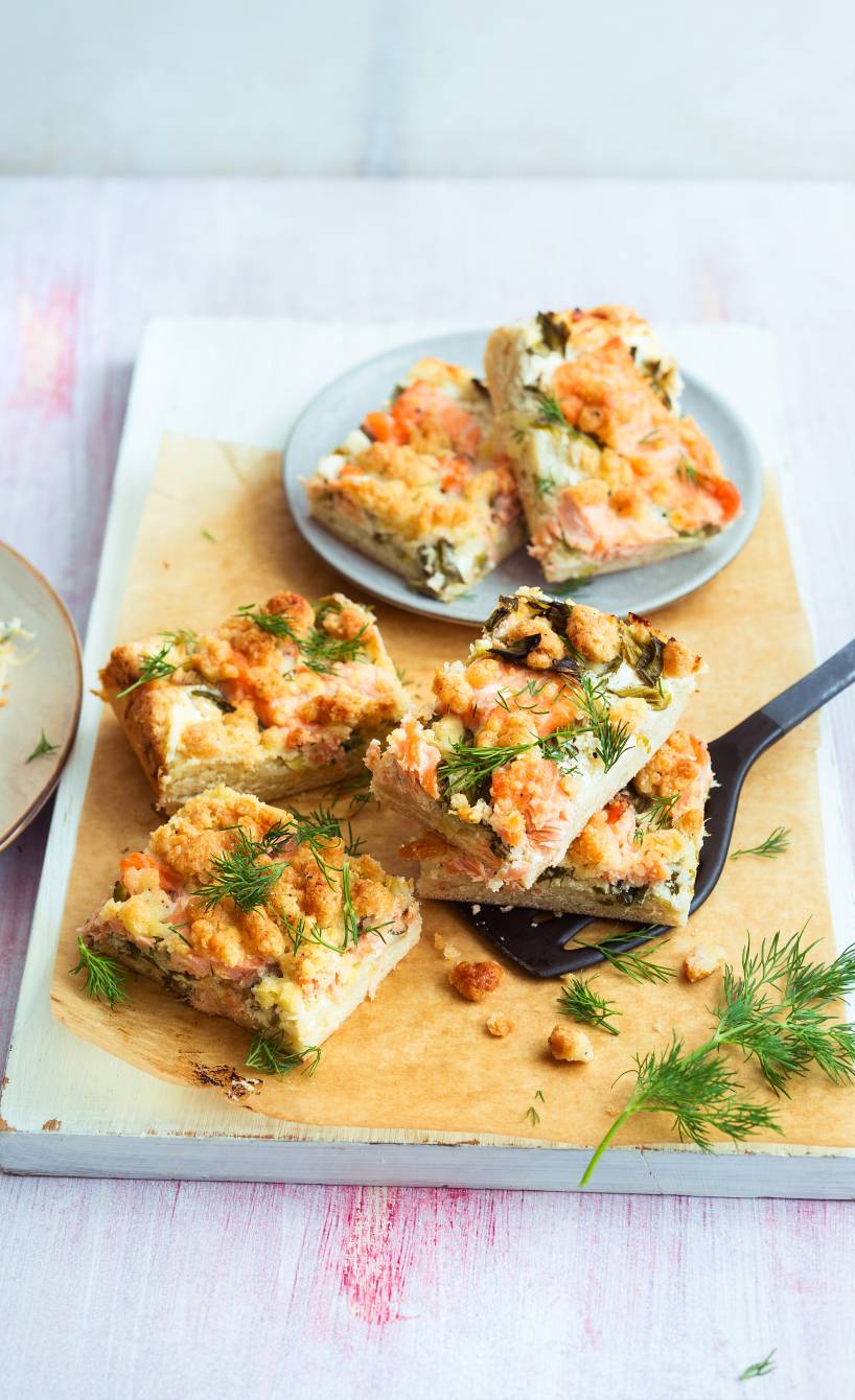Stücke vom Lachskuchen gestapelt auf einem Holzbrett getoppt mit Dillzweigen