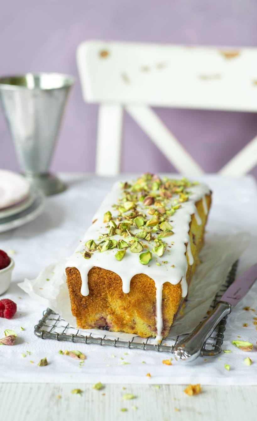 Selbstgebackener Mascarpone-Kastenkuchen mit Himbeeren getoppt von Zitronenguss und Pistazien auf einem Kuchengitter