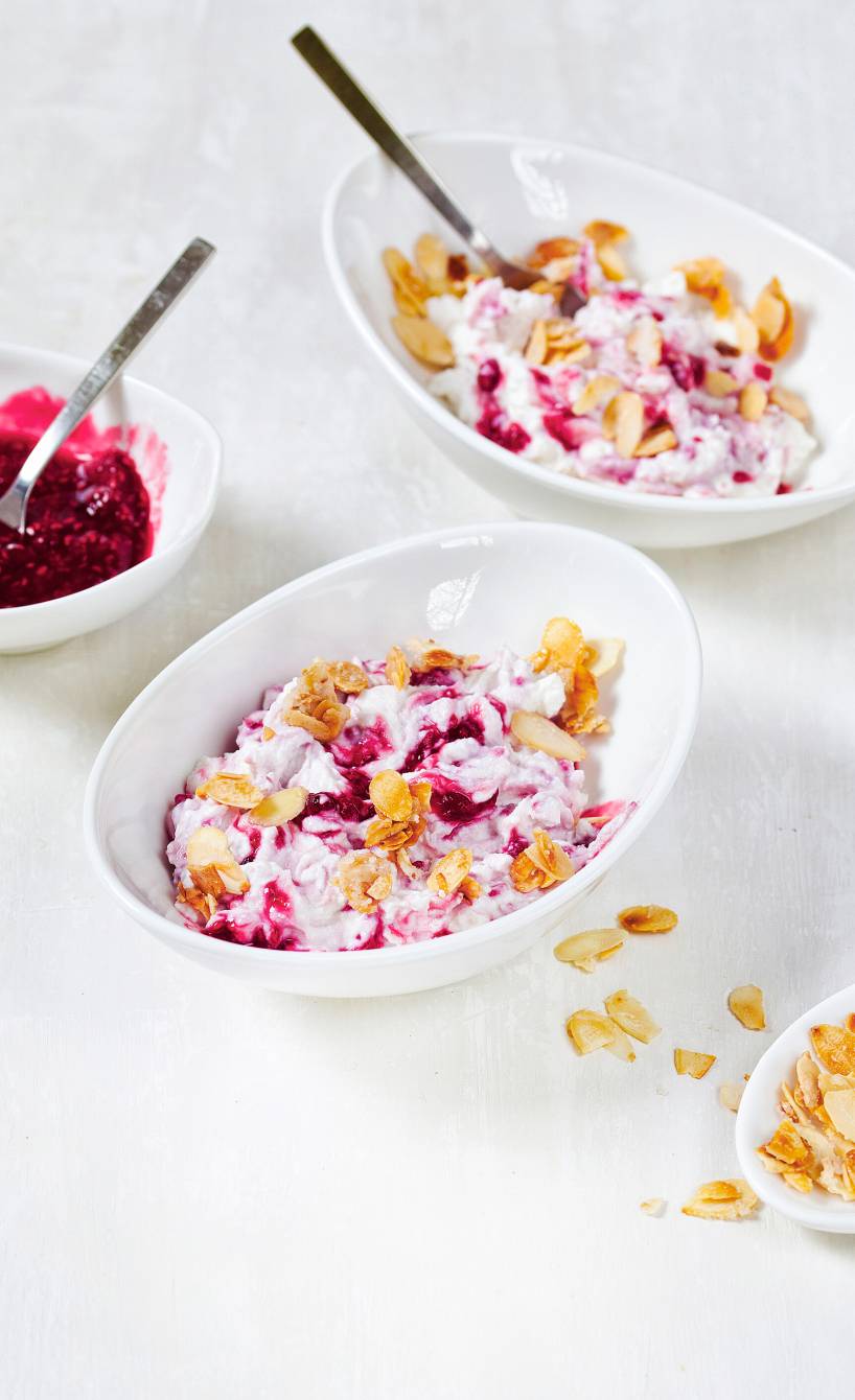Himbeer-Ricotta-Creme in mehreren Dessertschälchen getoppt von karamellisierten Mandelblättchen auf einem Tisch