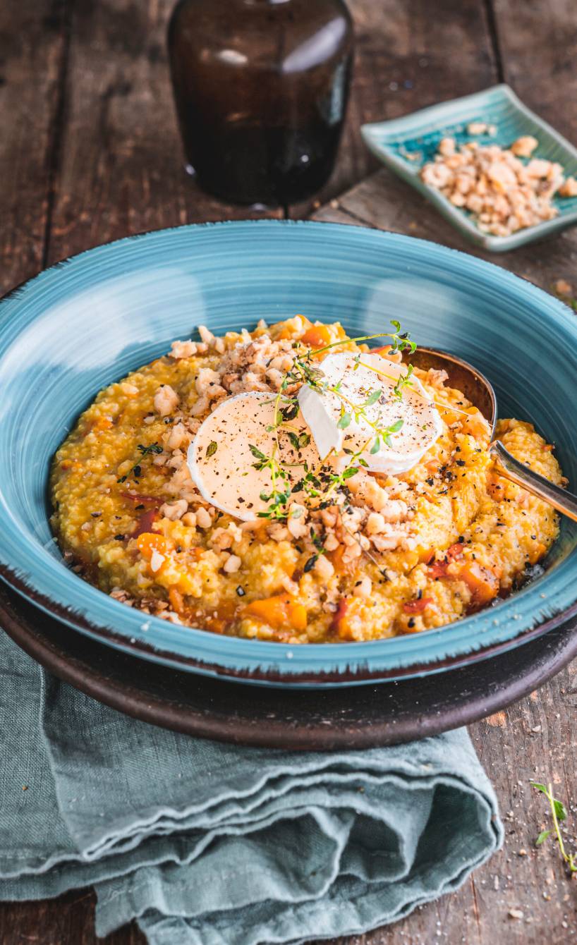 Hirsotto Risotto aus Hirse mit Karotten und Ziegenkäse angrichtet auf einem Teller getoppt von Walnüssen