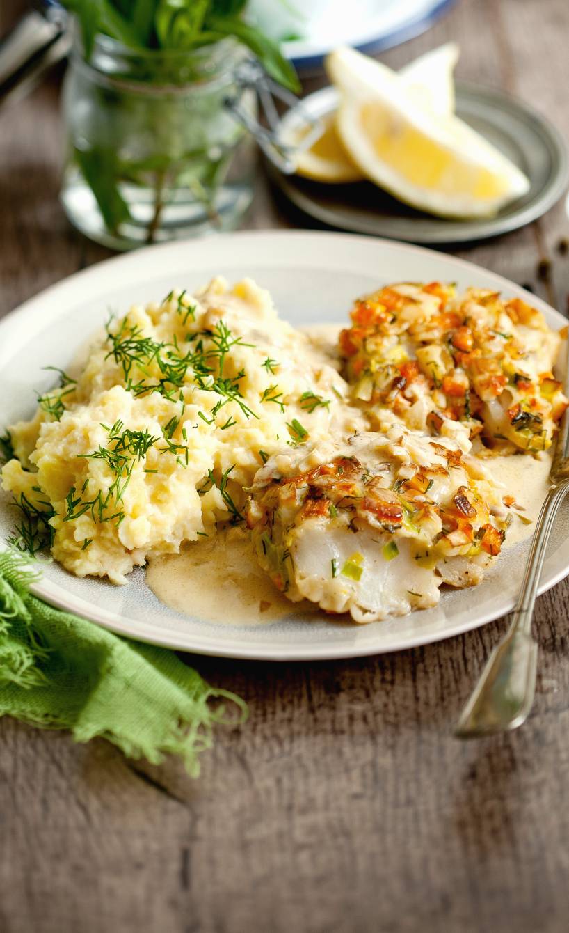 Gebratener, panierter Kabeljau auf einem Teller getoppt mit Estragonsauce, daneben Zitronenviertel