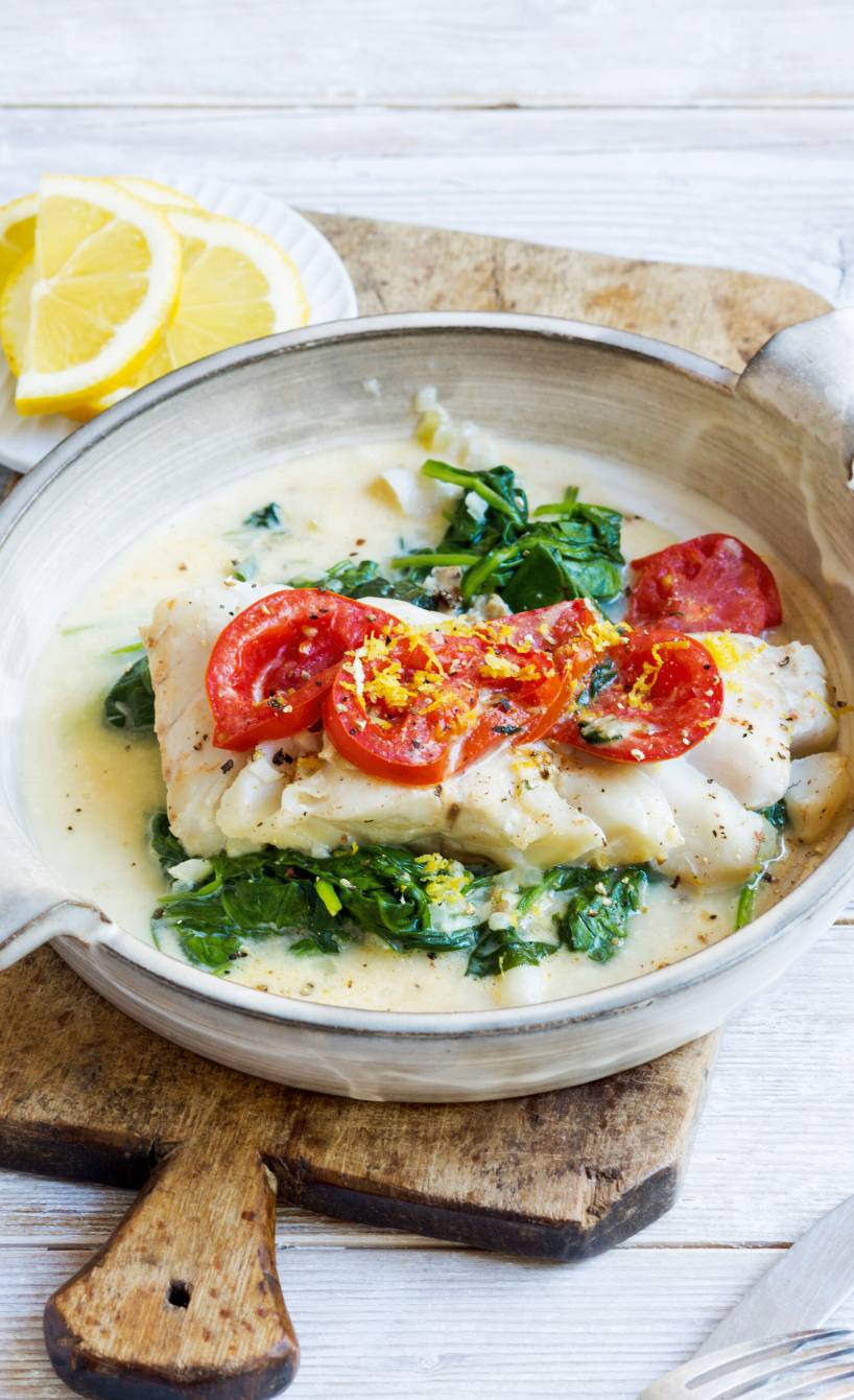 Kabeljau auf Rahmsppinat getoppt von Tomaten und geriebener Zitronenschale in einer Pfanne