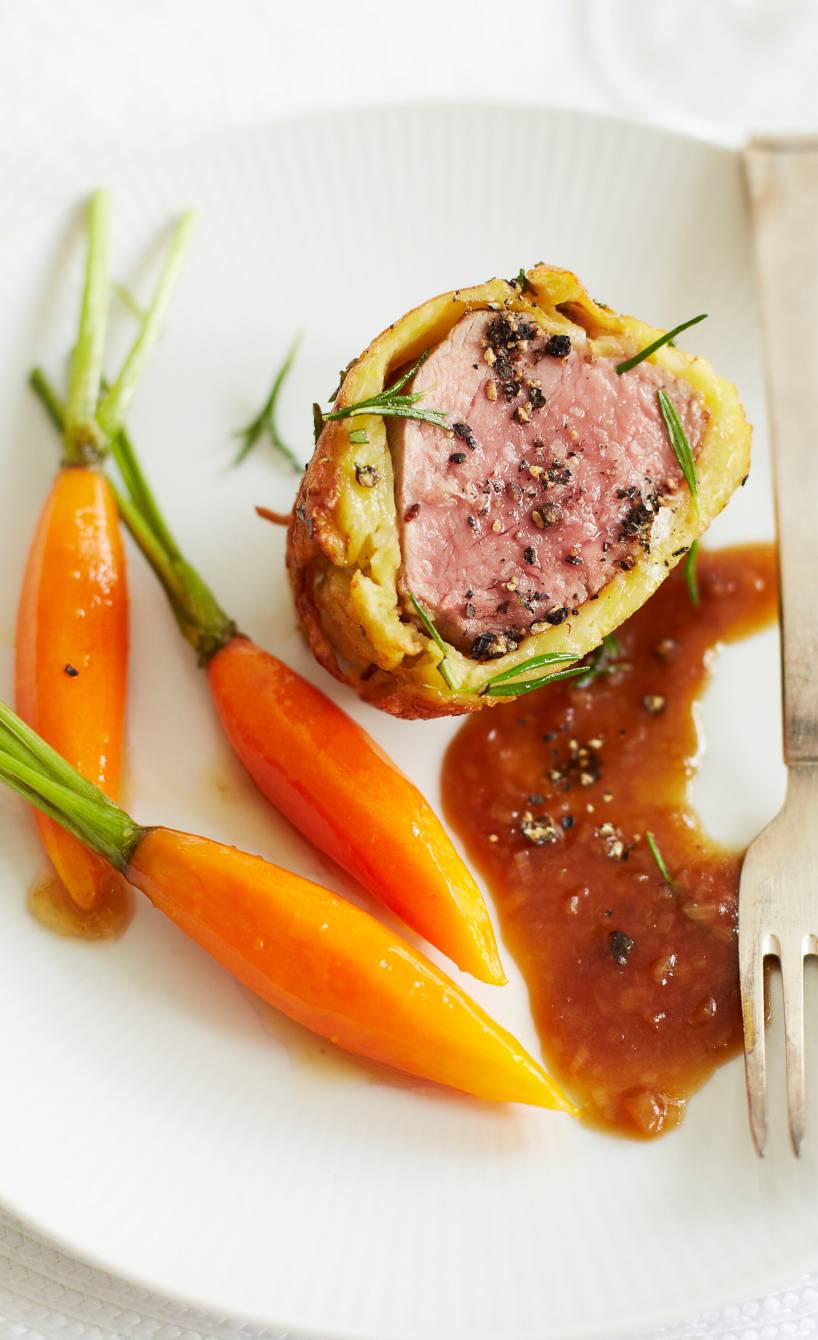 Ein Stück Kalbsfilet im Kartoffelmantel angerichtet mit Honig-Karotten und dunkler Sauce auf einem Teller