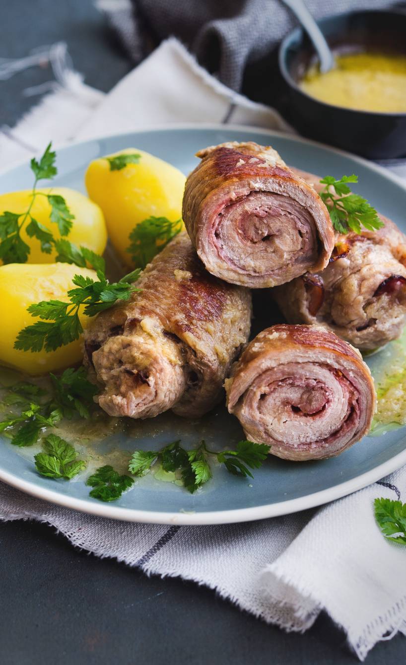 Italienische Kalbsrouladen mit Pancetta und Käse auf einem Teller, daneben Salzkartoffeln und helle Sauce