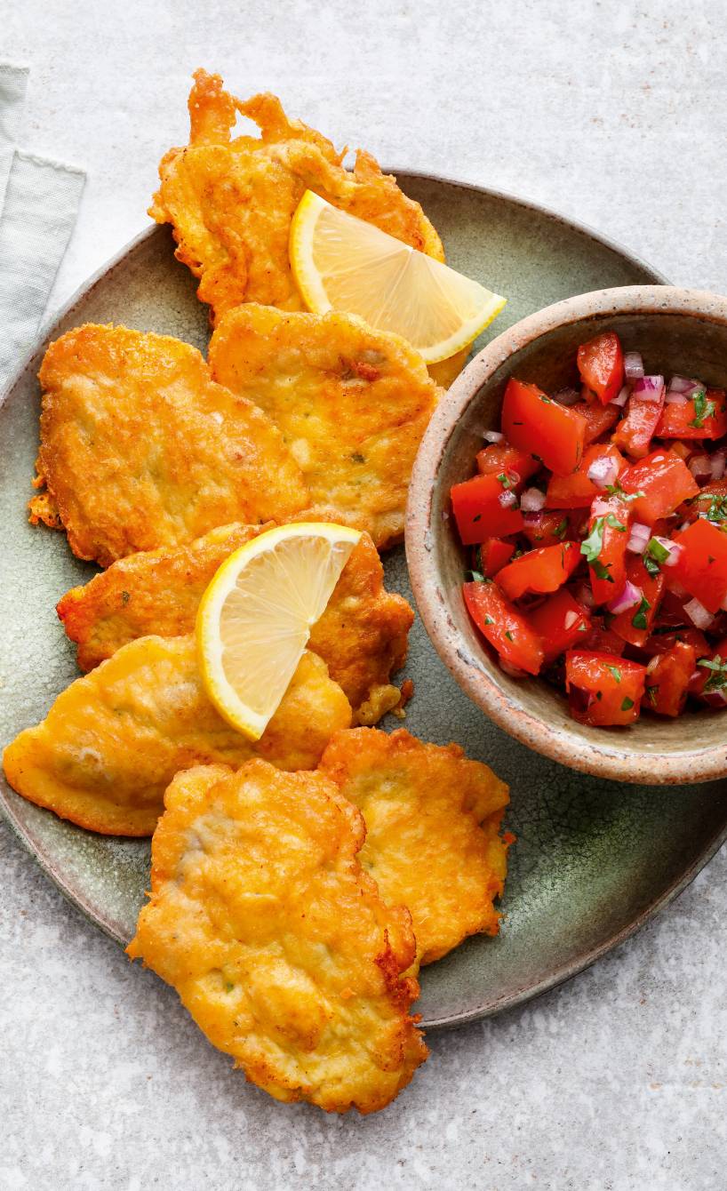 Mehrere Kalbsschnitzel in Parmesanpanade auf einem Teller mit einer Schale mit Tomatensalat