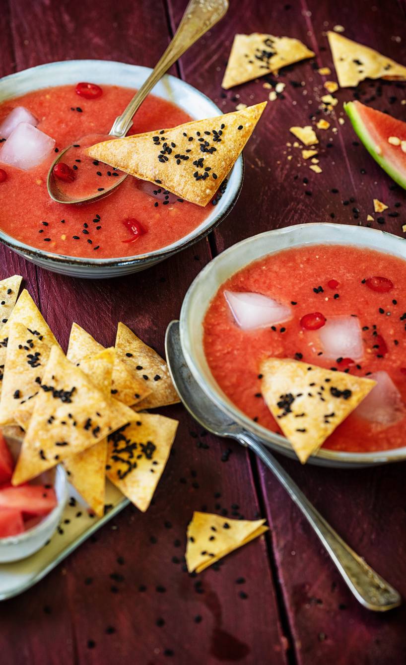 Tomatensuppe mit Eiswürfeln in zwei Schalen getoppt mit dreieckigen Crackern auf einem Tisch