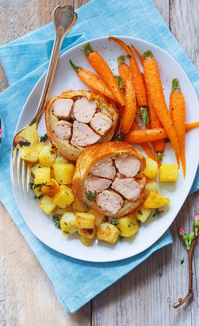 Gebackenes Kaninchenfilet im Brotmantel angerichtet auf einem Teller mit Thymiankartoffeln und ganzen, glasierten Karotten