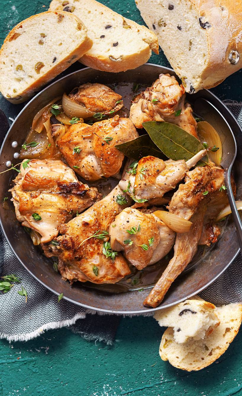 Geschmortes Kaninchen in einer Auflaufform, daneben selbstgebackenes Oliven-Ciabatta