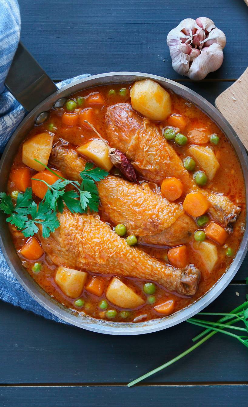 Kartoffeleintopf mit Hähnchen, Erbsen, Gemüse und Speck von oben in einem Topf, daneben angeschnittenes Baguette auf einem Holzbrett