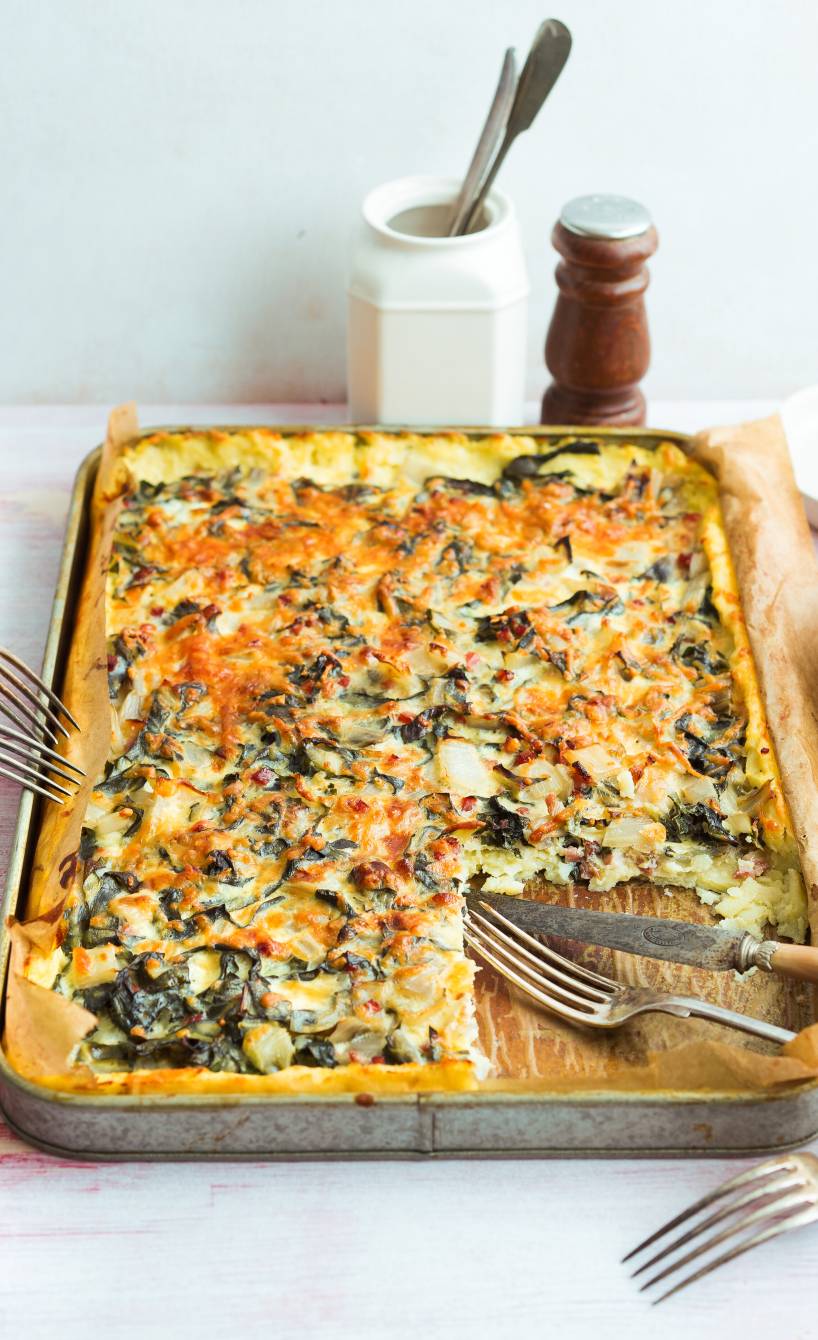 Glutenfreier Kartoffelkuchen mit Mangold und Speck angeschnitten auf einem Backblech