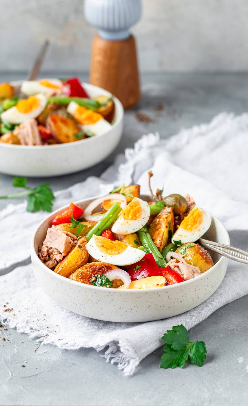 Italienischer Kartoffelsalat in zwei Salatschüsseln getoppt mit Eiern, grünen Bohnen und Thunfisch