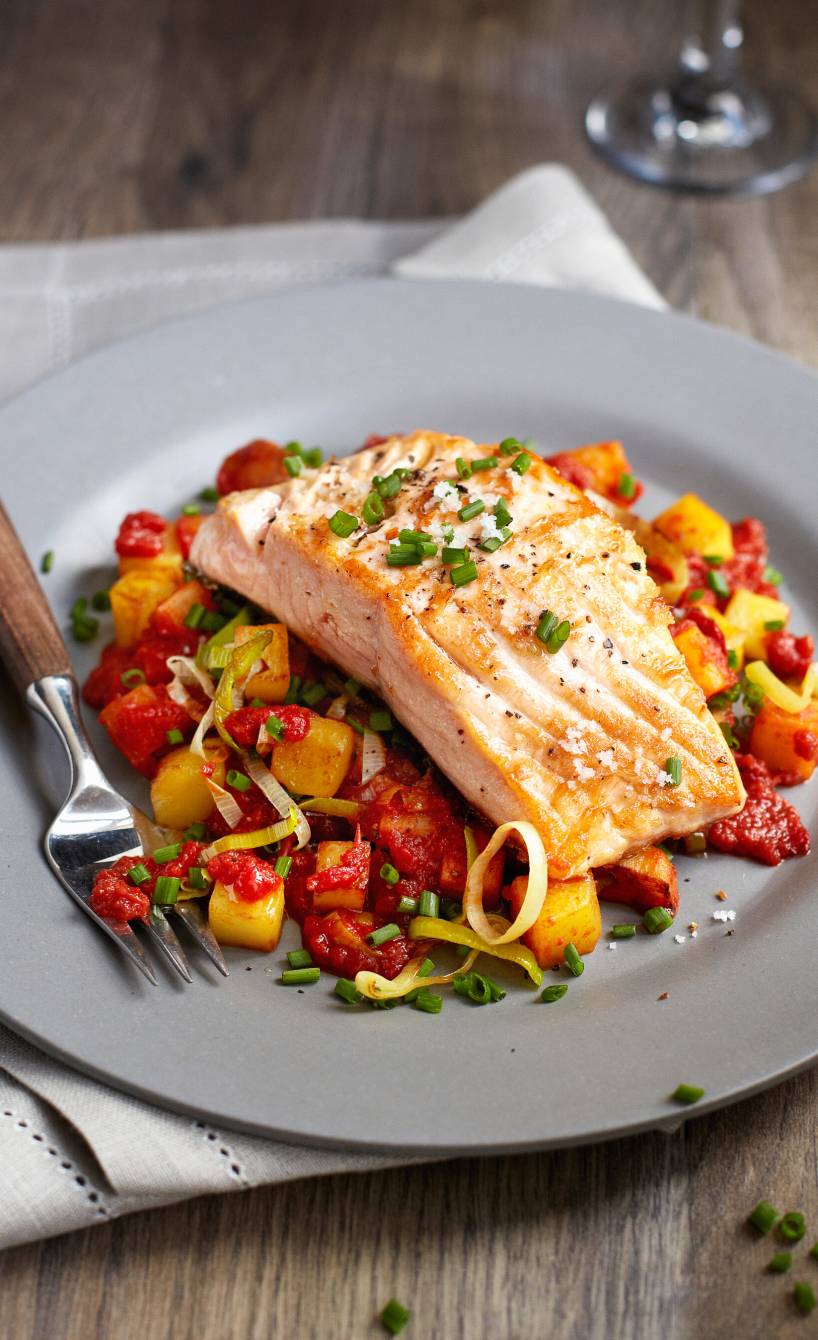 Kartoffelpfanne mit Gemüse auf einem Teller, darauf ein Stück gebratener Lachs