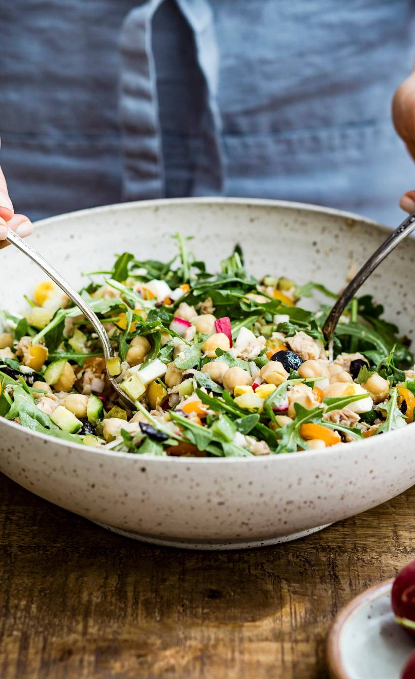 Bunter Thunfischsalat mir Kichererbsen wird gerade in einer Salatschüssel umgerührt