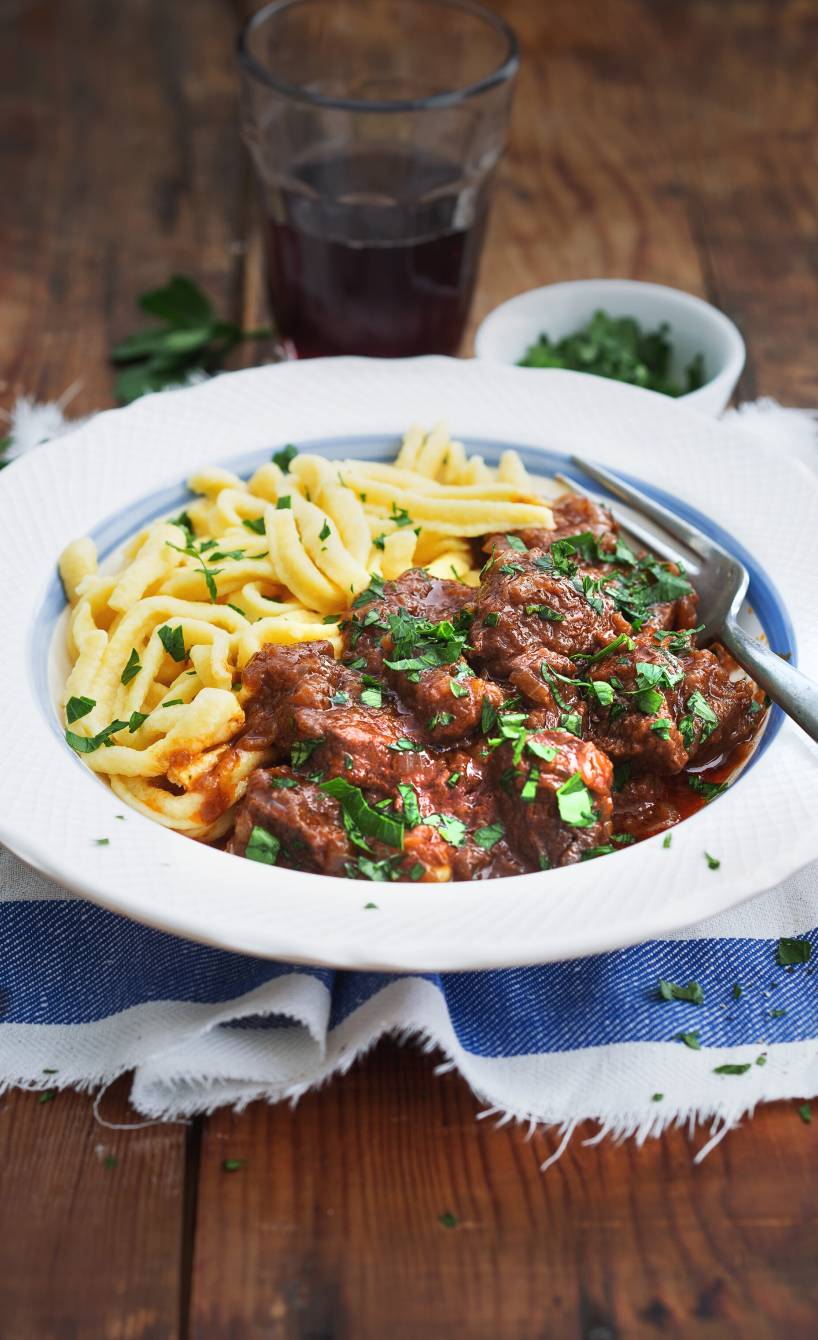 Rindergulasch mit Sauce bedeckt in einem tiefen Teller, daneben Spätzle