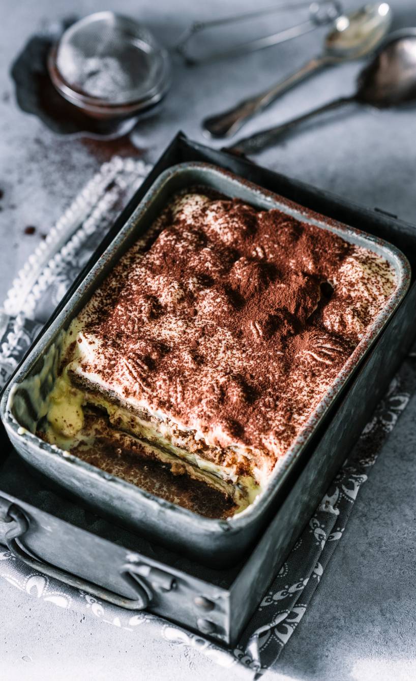 Tiramisu in einer metallenen Auflaufform angeschnitten auf einem Tisch