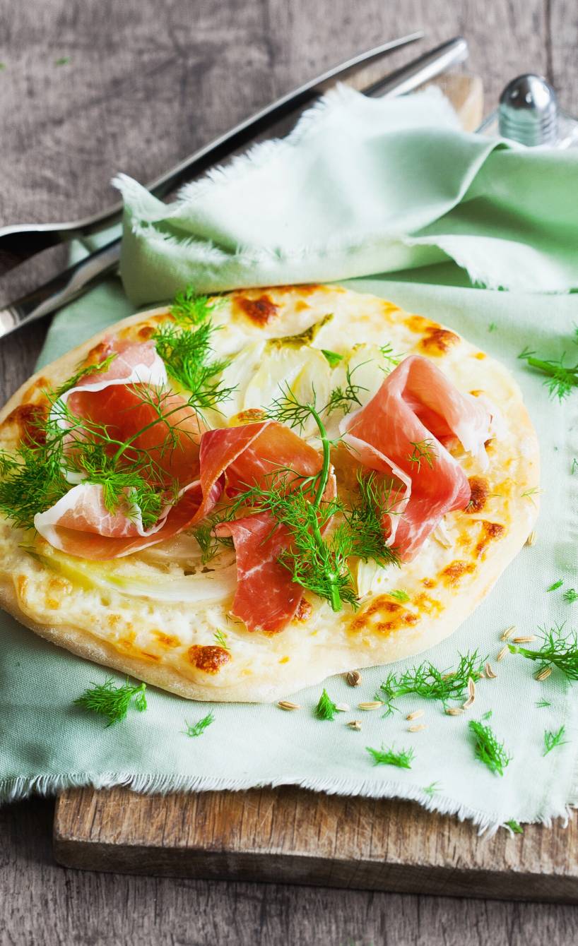 Fenchel-Pizza mit Schinken und Mozzarella auf einem Holzbrett