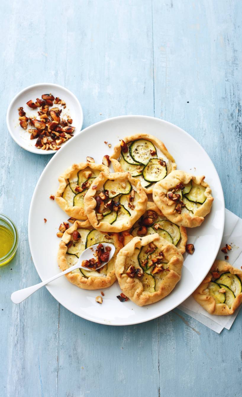 Sechs selbst gebackene Galettes belegt mit Zucchini und Ricotta getoppt von Gewürzmandeln auf einer Vorspeisenplatte