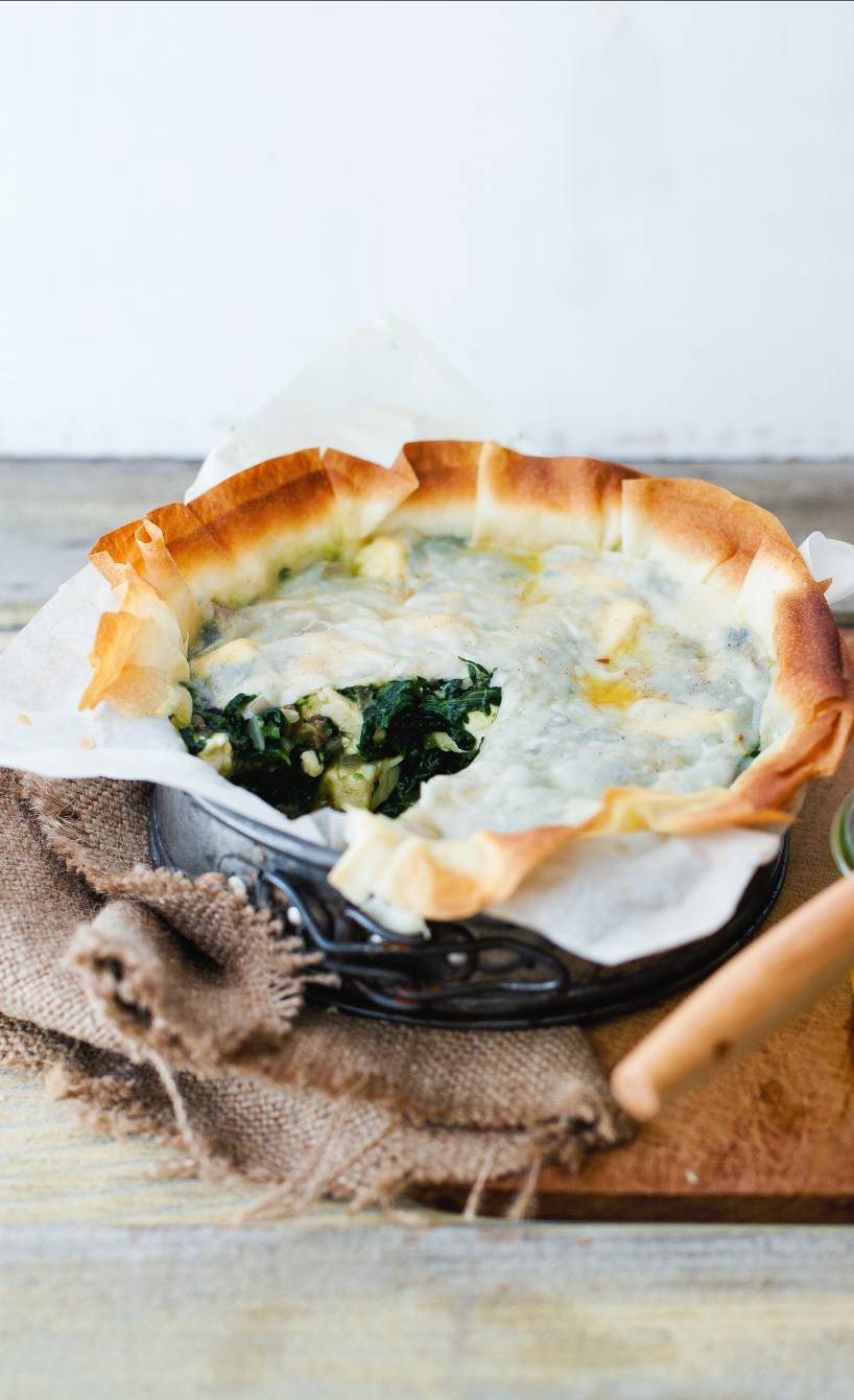 Selbstgebackener, angeschnittener Spinat-Feta-Kuchen mit Filoteig und Datteln in einer kleinen Springform auf einem Tisch
