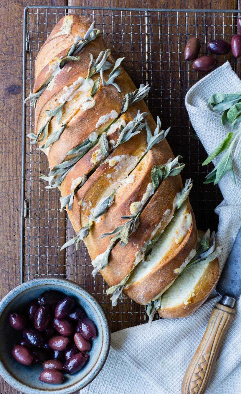 Selbst gebackenes Knoblauchbrot eingeschnitten und gefüllt mit Knoblauch, Parmesan und dekoriert mit Salbeiblättern auf einem Holztisch