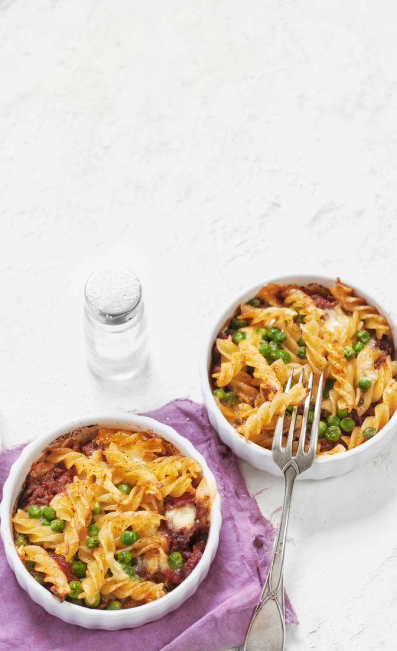 Fusilli mit Hackfleischragout und Erbsen in zwei kleinen runden Auflaufformen auf einem Tisch