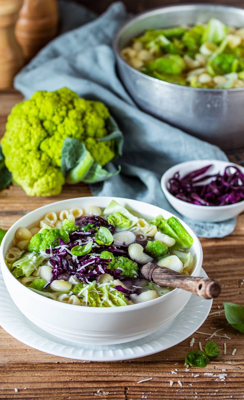 Minestrone mit verschiedenen Kohlsorten, Nudeln und Romanesco in einem Topf und einem Suppenteller auf einem Tisch