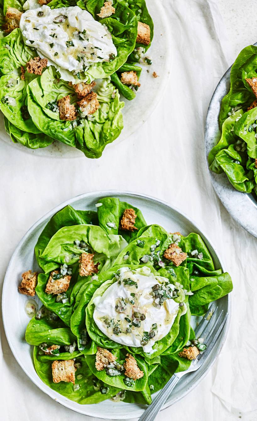 Grüner Salat auf drei Tellern getoppt von Burrata, Kapern und Stücken von Vollkornbaguette