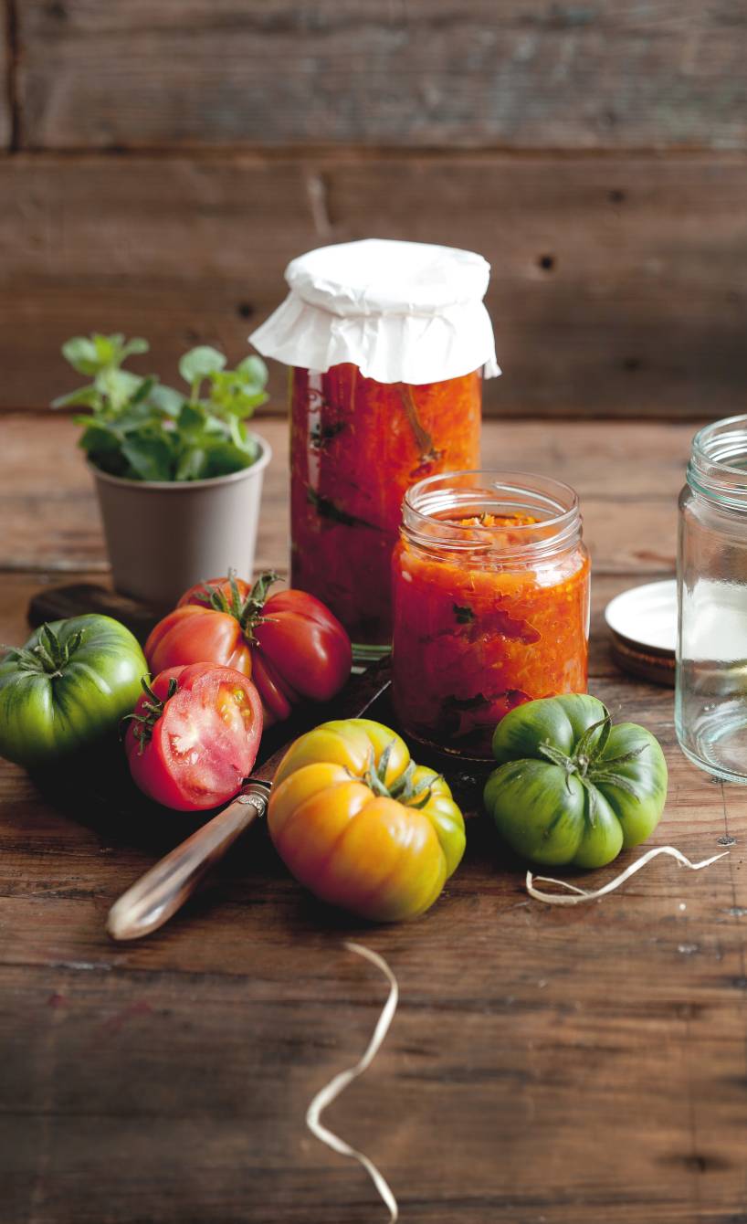 Tomatensoße in Schraubgläsern auf einem Holztisch, daneben Zutaten wie Tomaten